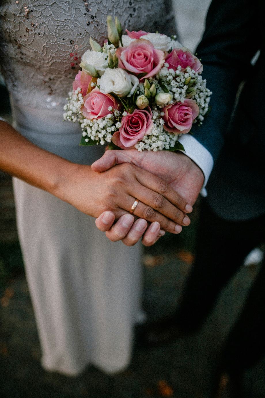 A couple holding hands with a bouquet of pink roses